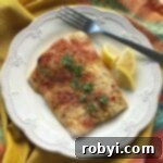 Baked Corvina with lemon crust on plate with fork and lemon wedges.