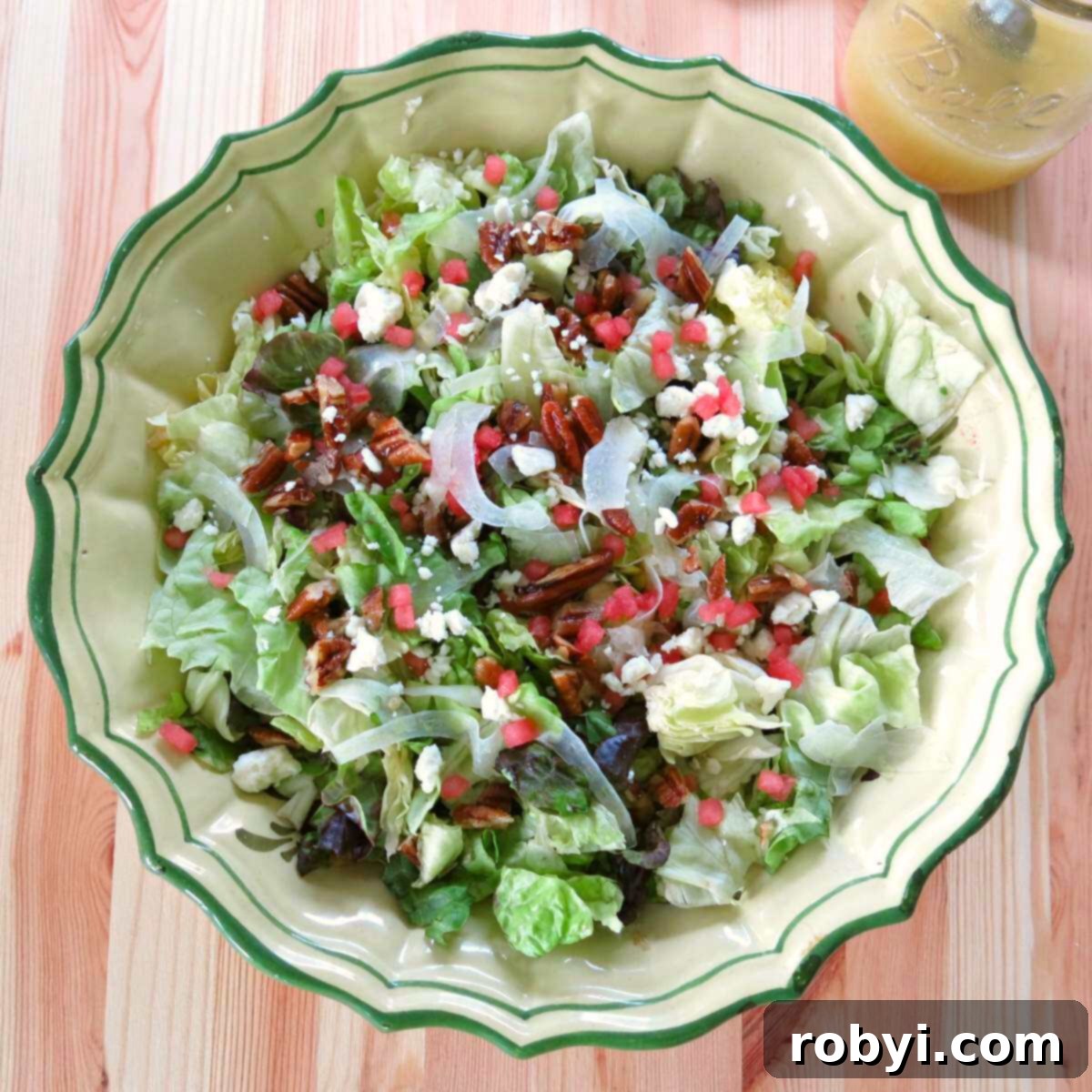 A beautifully presented bowl of Summer Fennel Salad featuring shaved fennel, vibrant watermelon cubes, crumbled feta, and glistening candied pecans. A mason jar of homemade Orange Honey Mustard Vinaigrette sits behind it, ready to be drizzled.