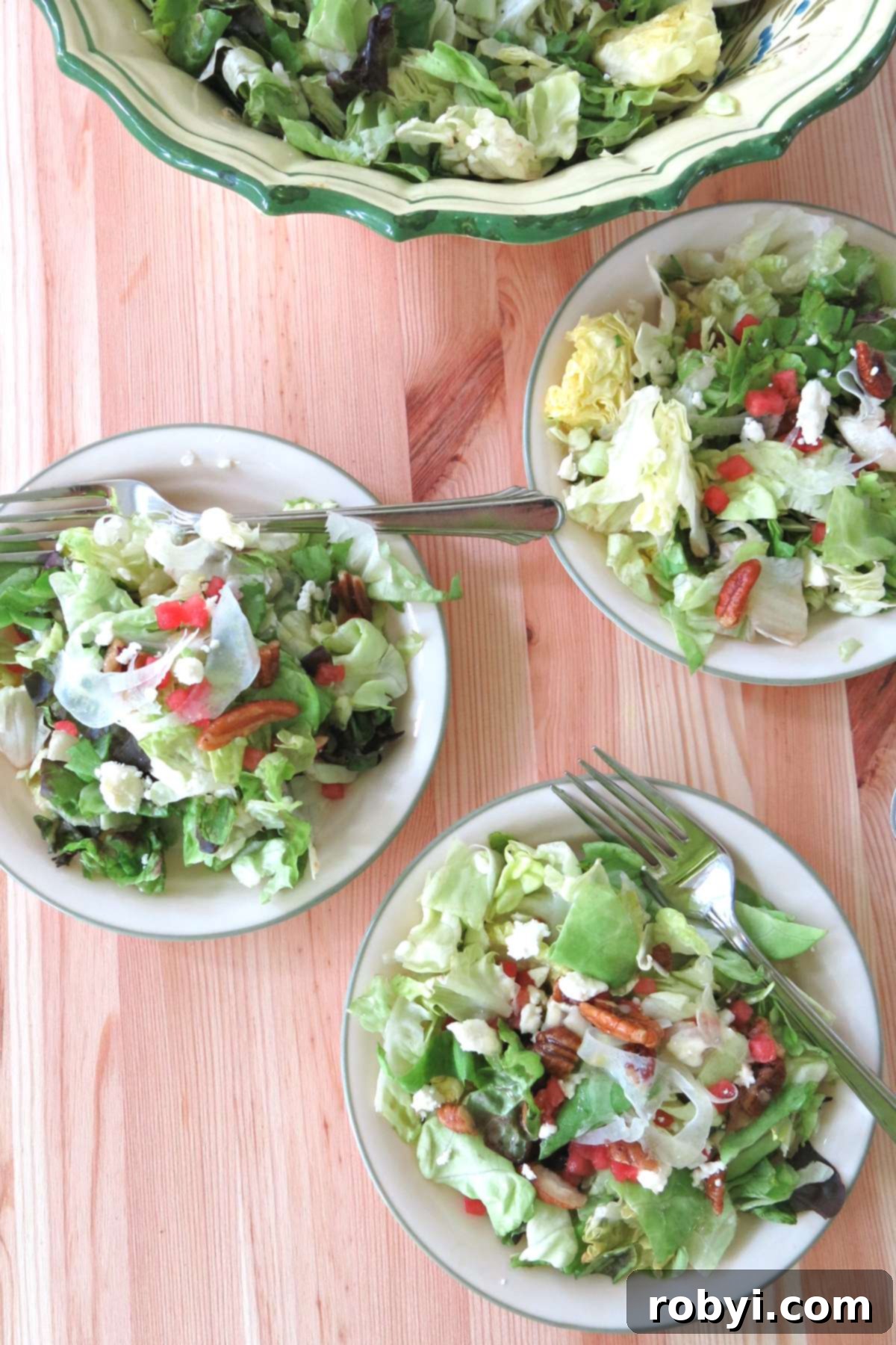 Three small, individual side salads featuring shaved fennel, glistening candied pecans, juicy watermelon cubes, and crumbled feta cheese, arranged on plates. A larger serving bowl of the same salad is visible in the background, illustrating elegant plating options.