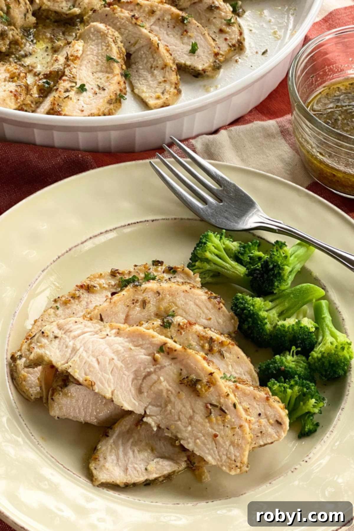 Plate with five slices of baked turkey tenderloin next to broccoli with a platter of more behind it.