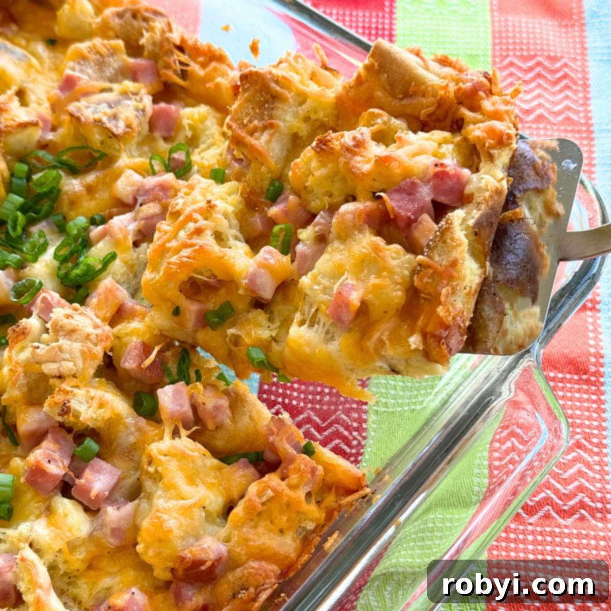 Spatula lifting a serving of ham strata out of the corner of a glass baking dish.