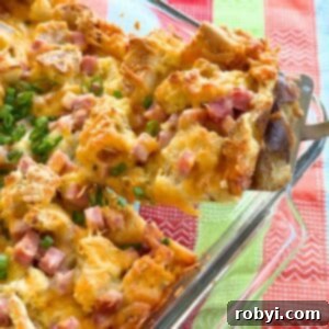 Spatula lifting a serving of ham strata out of the corner of a glass baking dish.