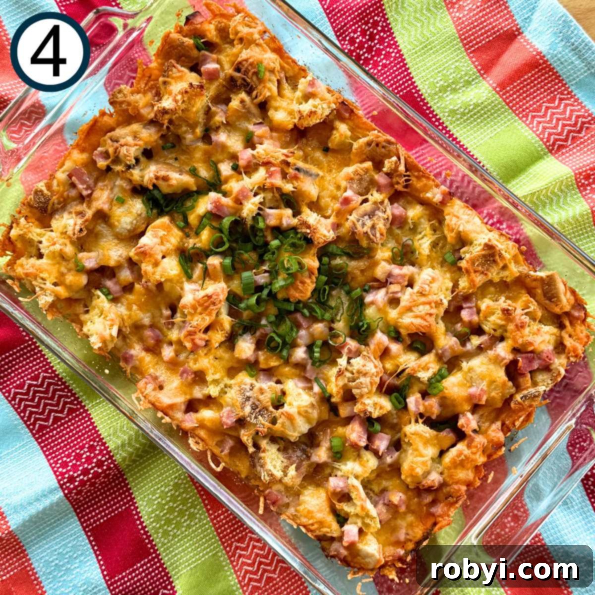 Cooked ham and cheese strata topped with sliced green onions (the green parts) in a 9 x 12 baking dish on a colorful pastel napkin.