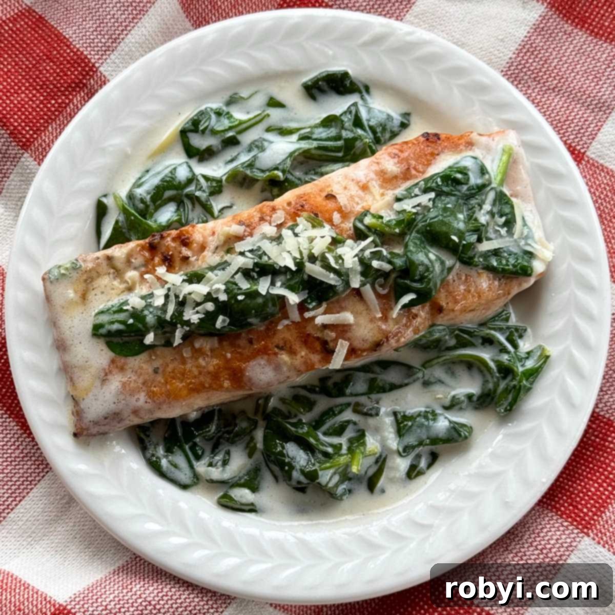 A vibrant serving of salmon florentine with a creamy spinach sauce, garnished with fresh parsley on a white plate.