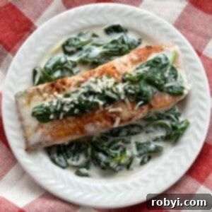 A serving of salmon florentine with a creamy spinach sauce on a white plate.