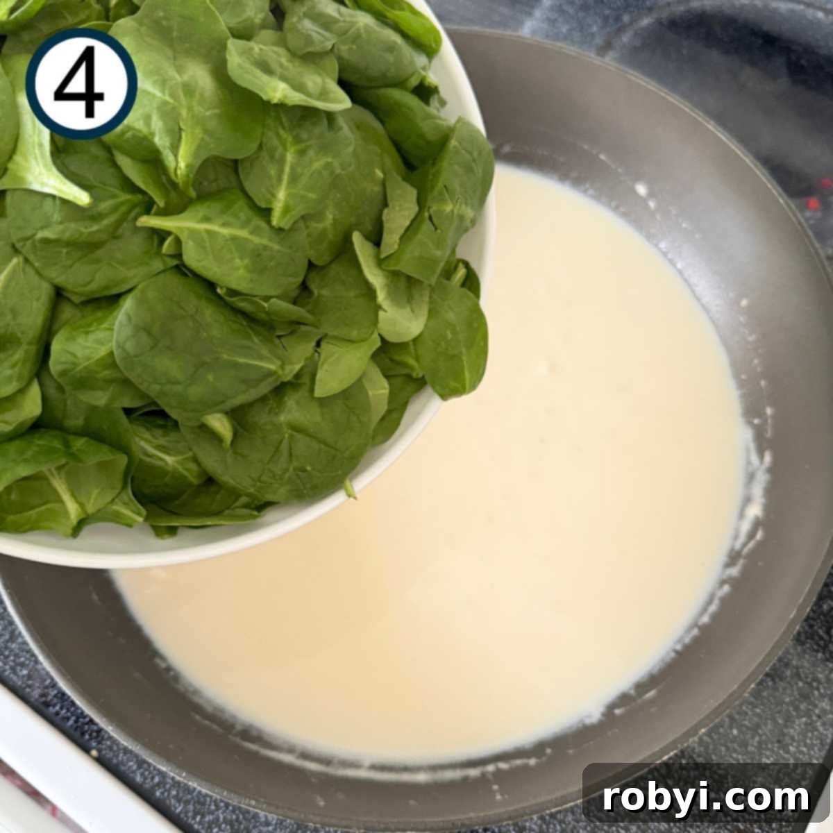 Fresh baby spinach leaves being added to the skillet with the Parmesan cream sauce.