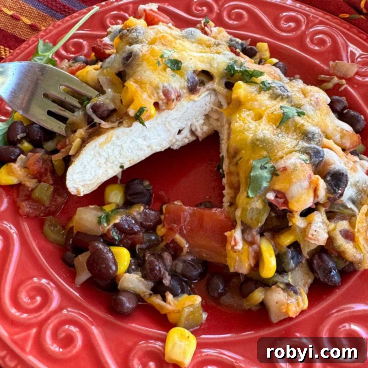 Chuckwagon Chicken Dinner 2 Serving of cowboy chicken that has been cut in half on a red plate, showcasing the tender chicken, vibrant corn and black bean salsa, and melted cheese.