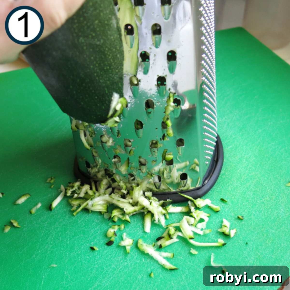 Decadent Zucchini Chocolate Brownies 4 A hand is actively grating a vibrant green zucchini using the large holes of a box grater, creating delicate shreds.