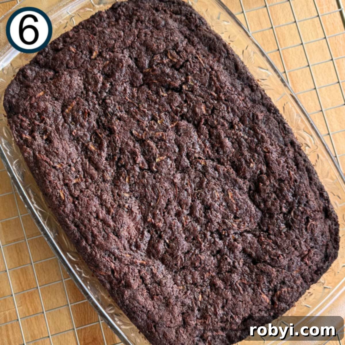 Decadent Zucchini Chocolate Brownies 9 A freshly baked batch of fudgy zucchini brownies, still warm, sits in a glass baking dish on top of a wire rack, ready to cool.