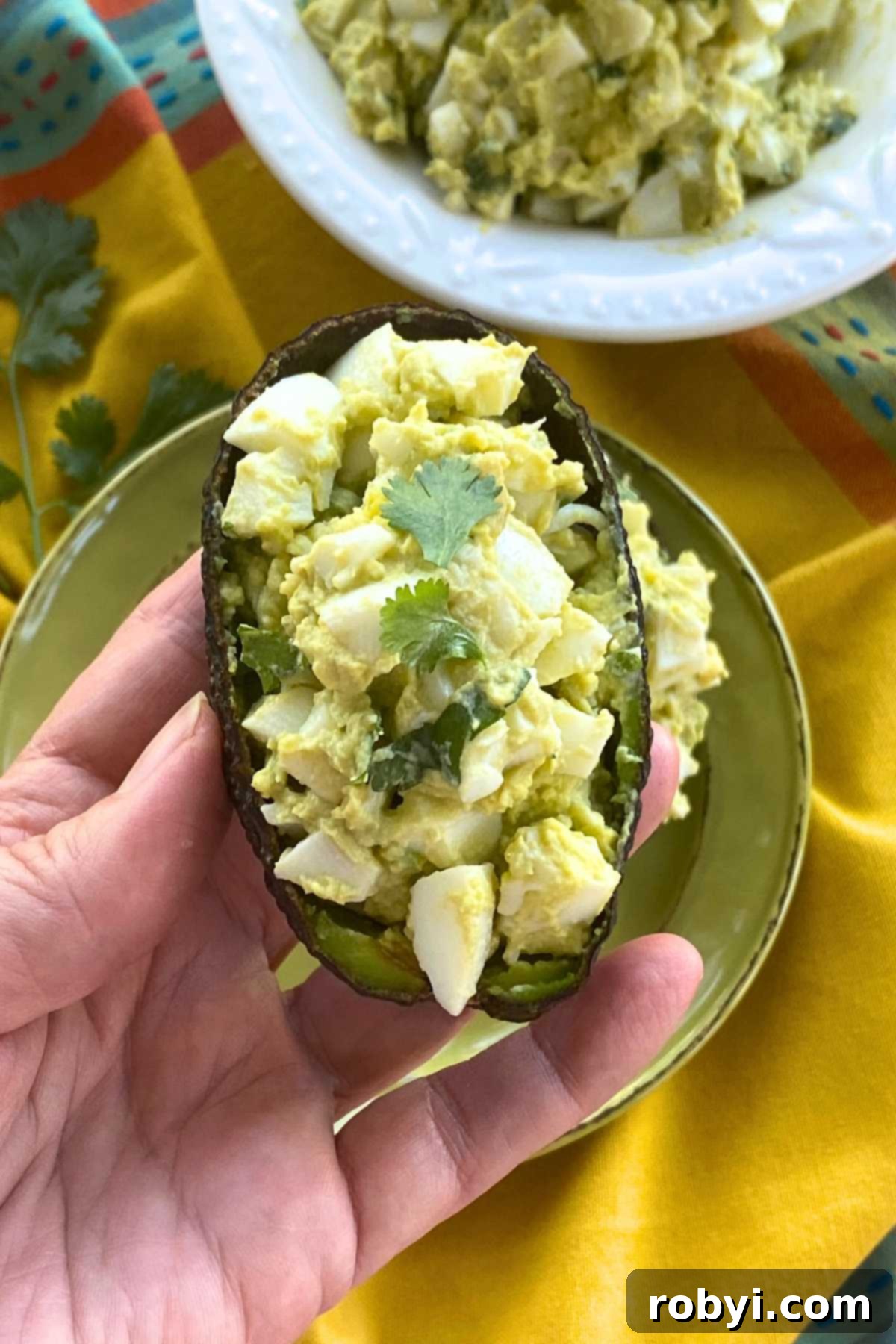 Bright and Light Egg Salad 8 Hand holding a scooped out avocado half filled with healthy egg salad.