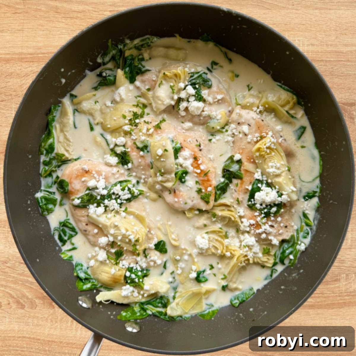 Spinach artichoke chicken in a skillet covered in a creamy lemon sauce and topped with goat cheese.