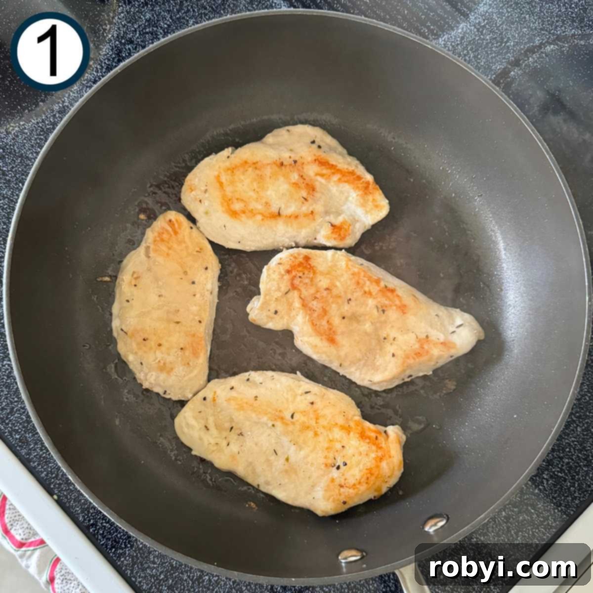 Four browned chicken cutlets in a skillet.