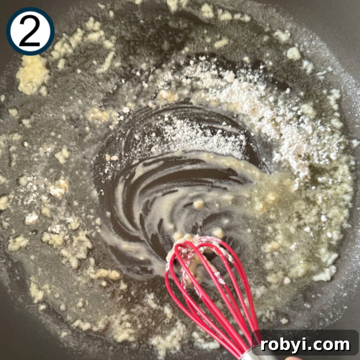 Garlic, butter, and flour being whisked in a skillet.
