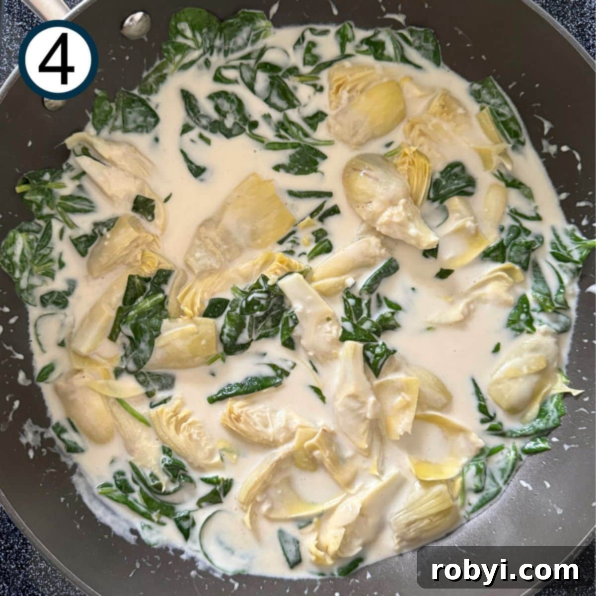 Spinach and artichokes mixed into lemon cream sauce in a large skillet.