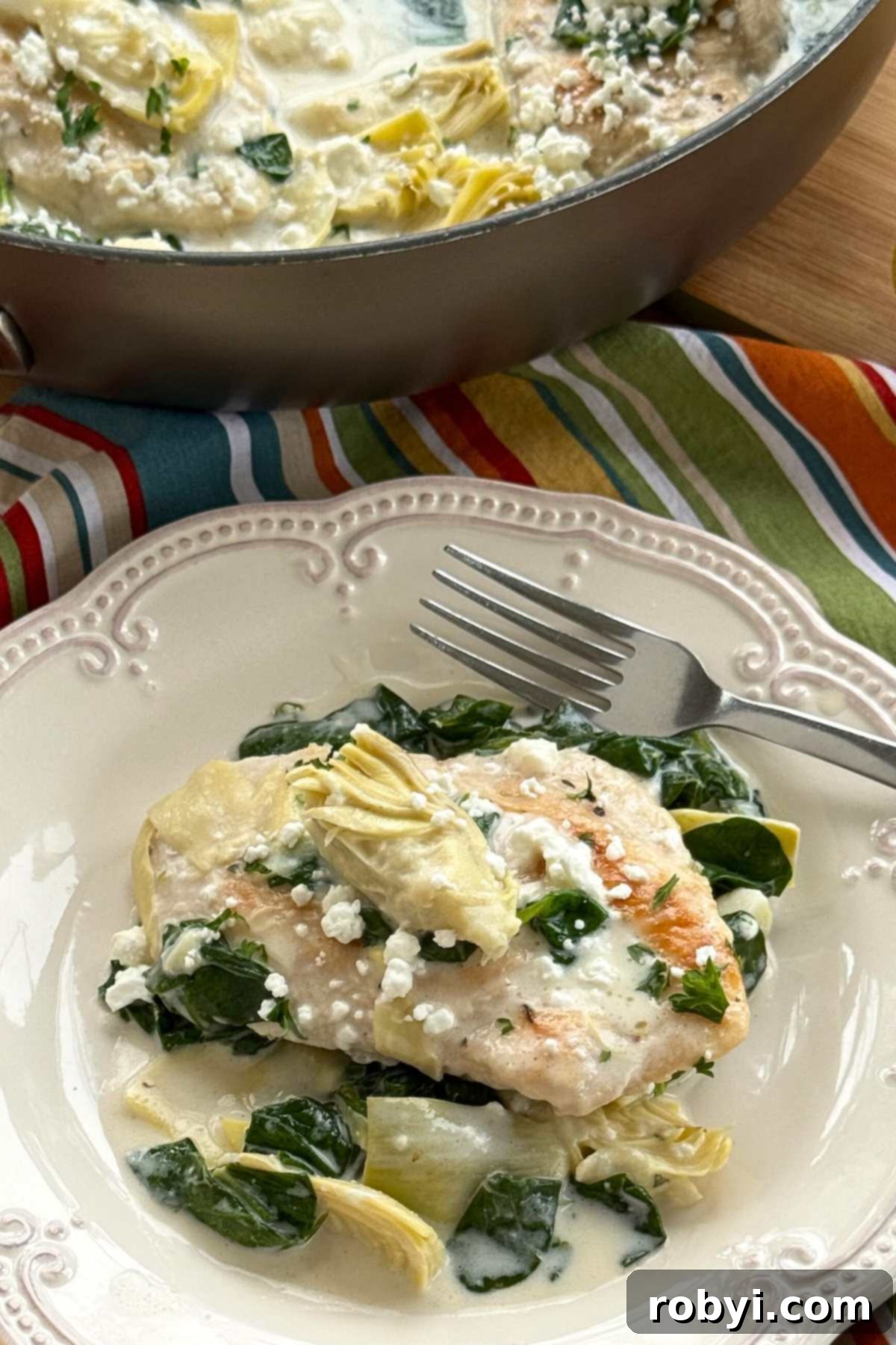 Serving of chicken with spinach and artichokes in a lemon cream sauce topped with goat cheese.