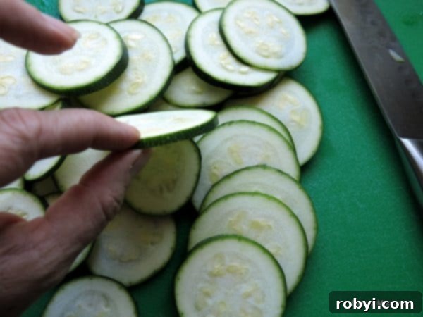 fingers holding Sliced Zucchini with lots of rounds on cutting board.