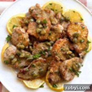 Pork tenderloin picatta with a a lemon caper sauce on a white plate surrounded by lemon slices.