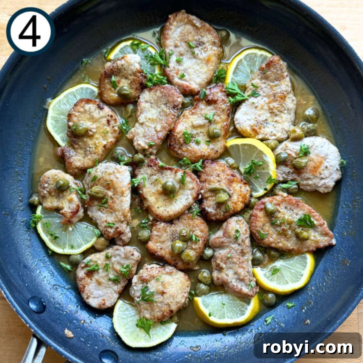 Skillet with cooked chicken piccata with lemon slices tucked around the edges and fresh parsley sprinkled over the top.
