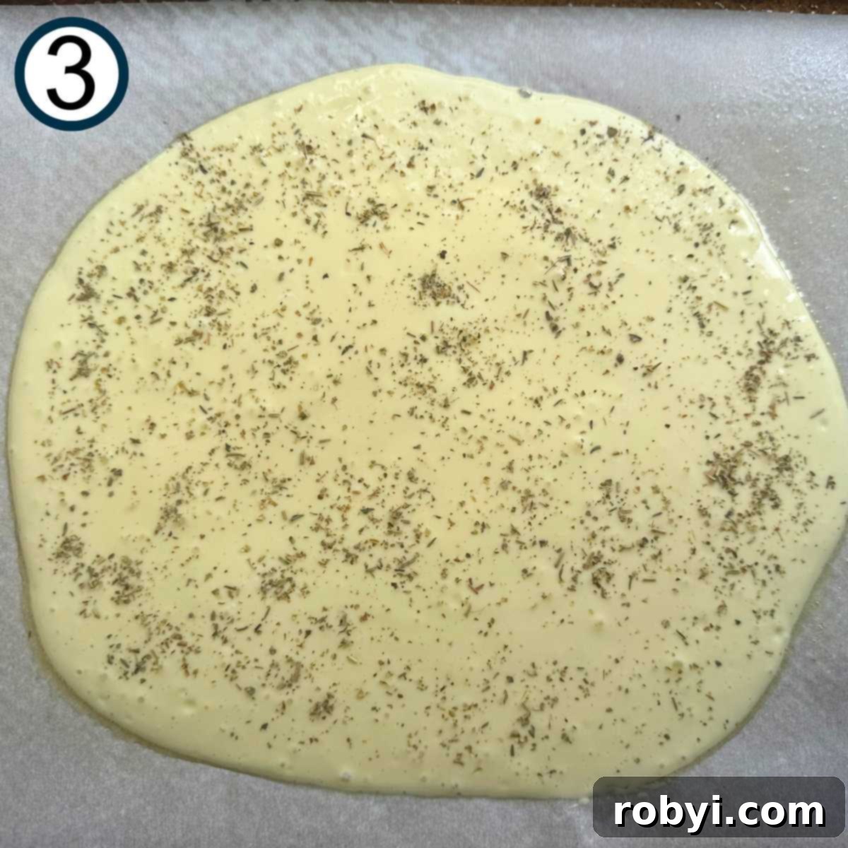 Cottage cheese flatbread batter sprinkled with Italian seasoning on parchment paper before baking.