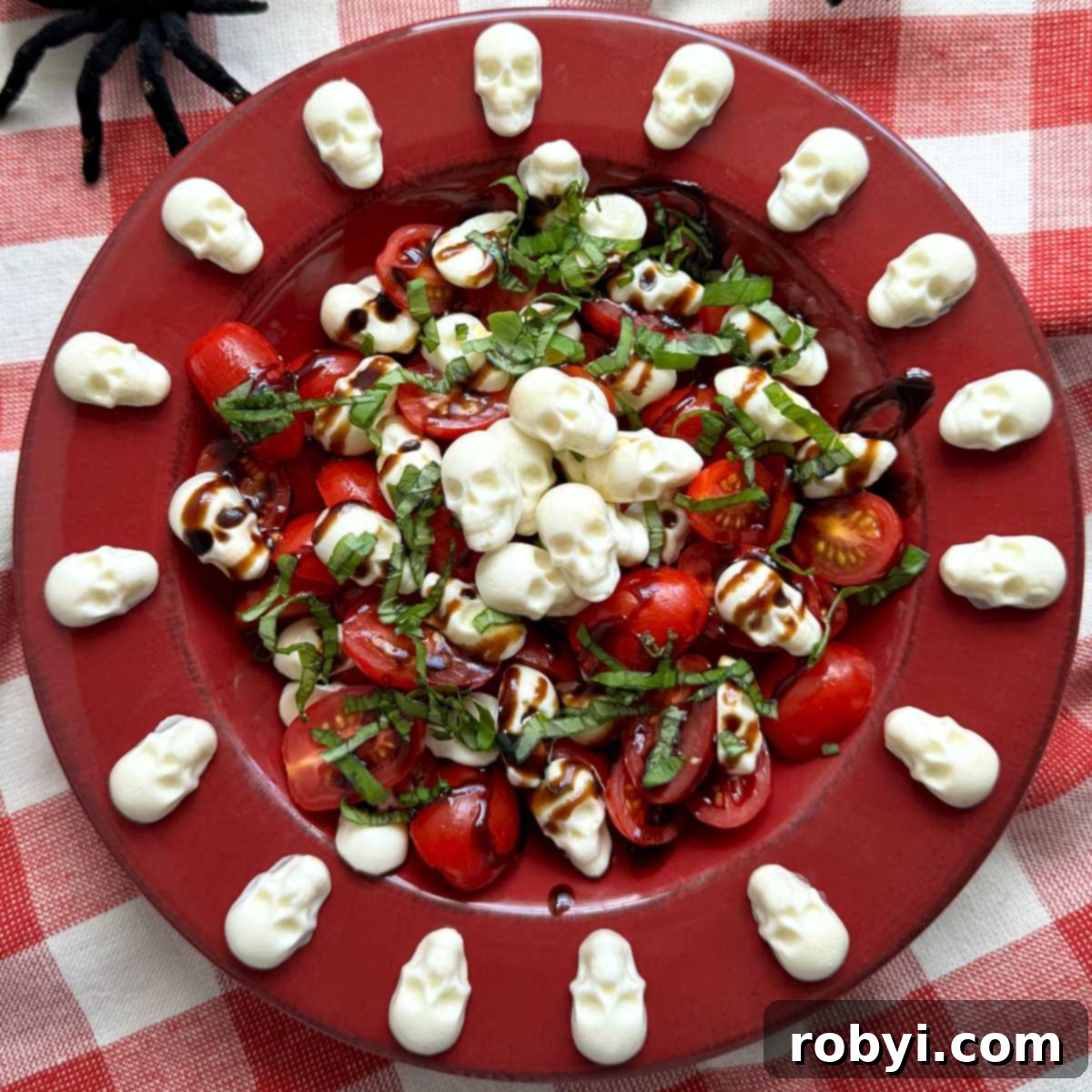 A festive red bowl showcasing Halloween Caprese Salad, adorned with eerie mozzarella skulls arranged around the rim and piled in the center, creating a spooky and delicious display.