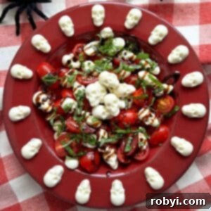 A striking red bowl filled with Halloween Caprese Salad, featuring spooky mozzarella skulls gracefully arranged around the flat rim of the bowl.