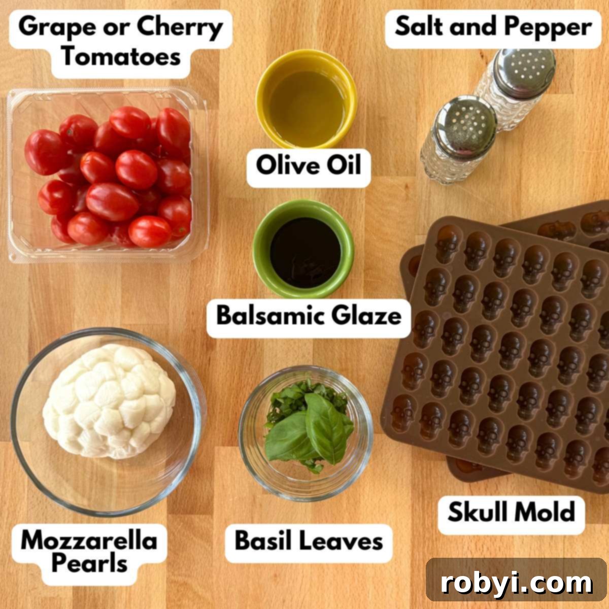 A flat lay photograph displaying all the ingredients for Halloween Caprese Salad: vibrant grape tomatoes, creamy mozzarella pearls, a bottle of rich balsamic glaze, olive oil, fresh basil leaves, a skull candy mold, and a sprinkle of salt and pepper.