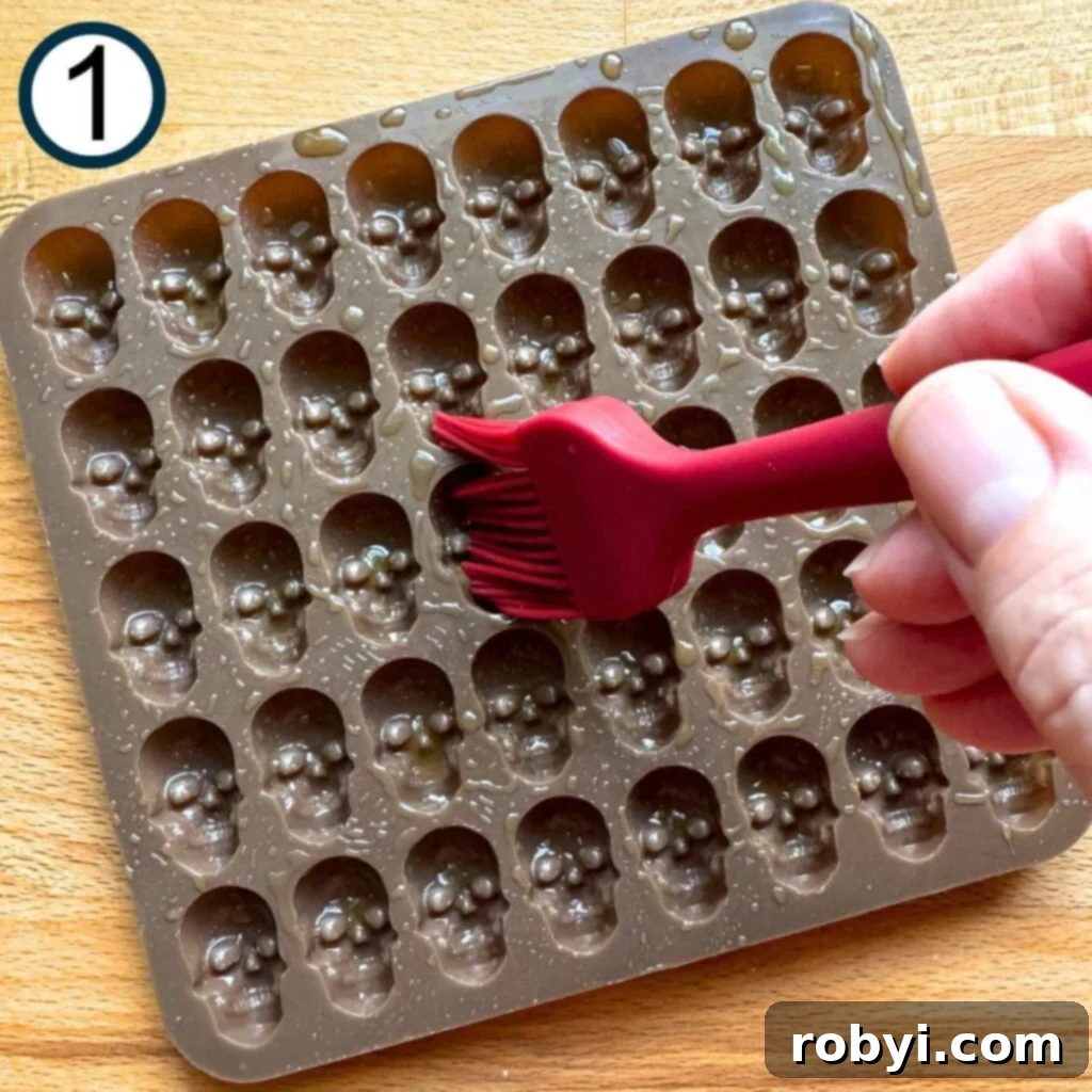 A hand delicately brushes olive oil into the intricate cavities of a skull candy mold, preparing it for the mozzarella.