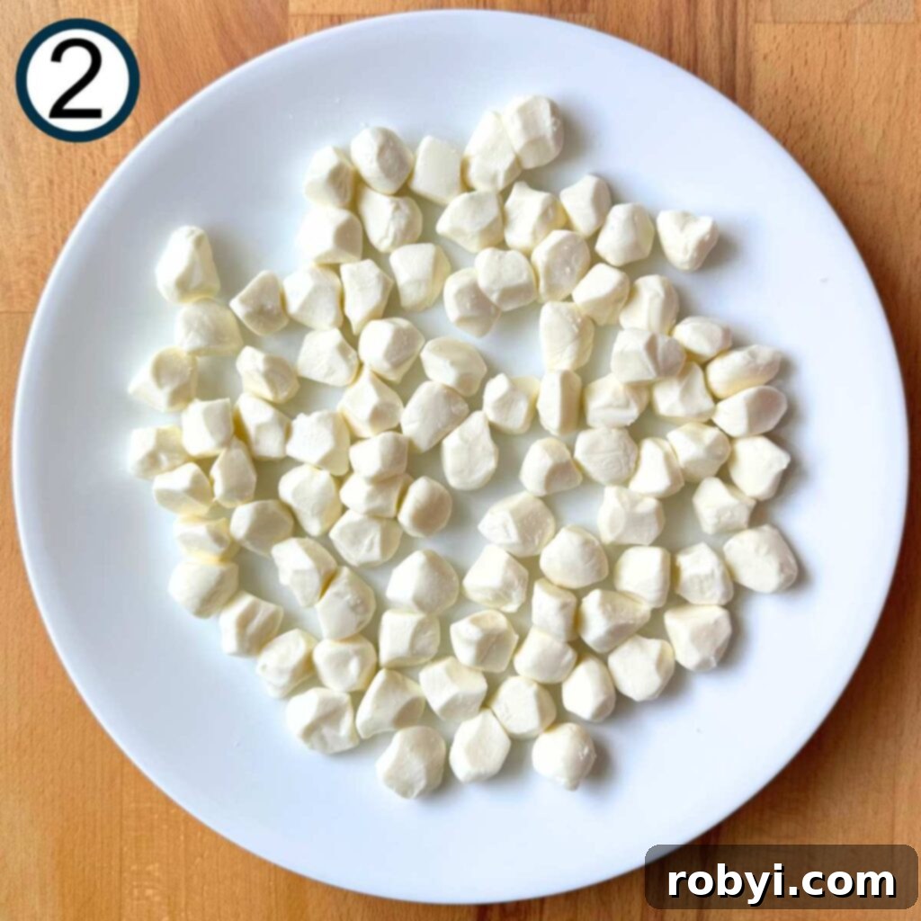 Fresh mozzarella pearls are spread evenly on a white, microwave-safe plate, ready for softening.