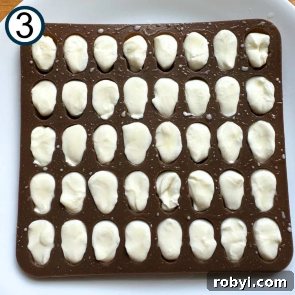 Softened mozzarella is carefully pressed into the greased skull candy mold, showing the detailed shape beginning to form.