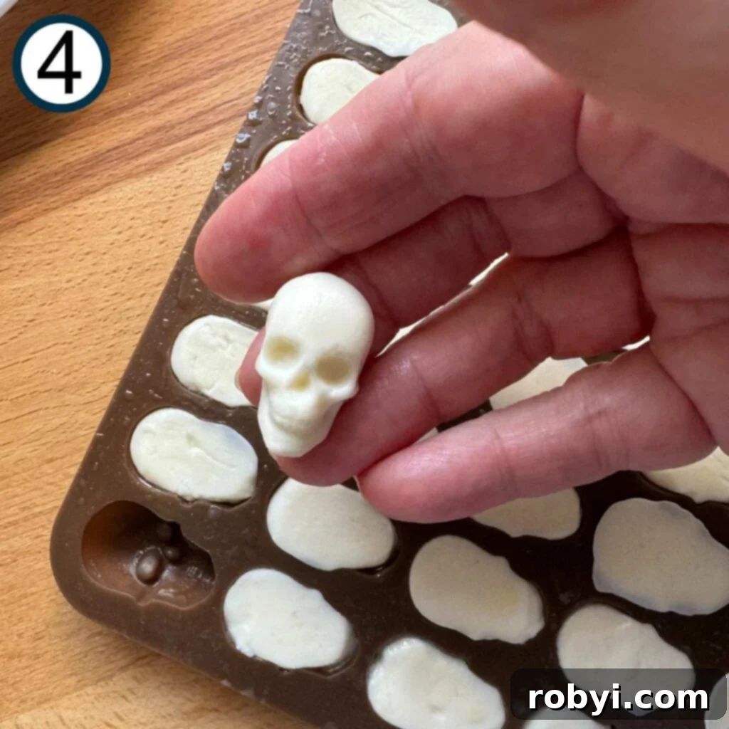 Fingers gently holding a freshly molded mozzarella skull, with the silicone mold visible below, ready for chilling.