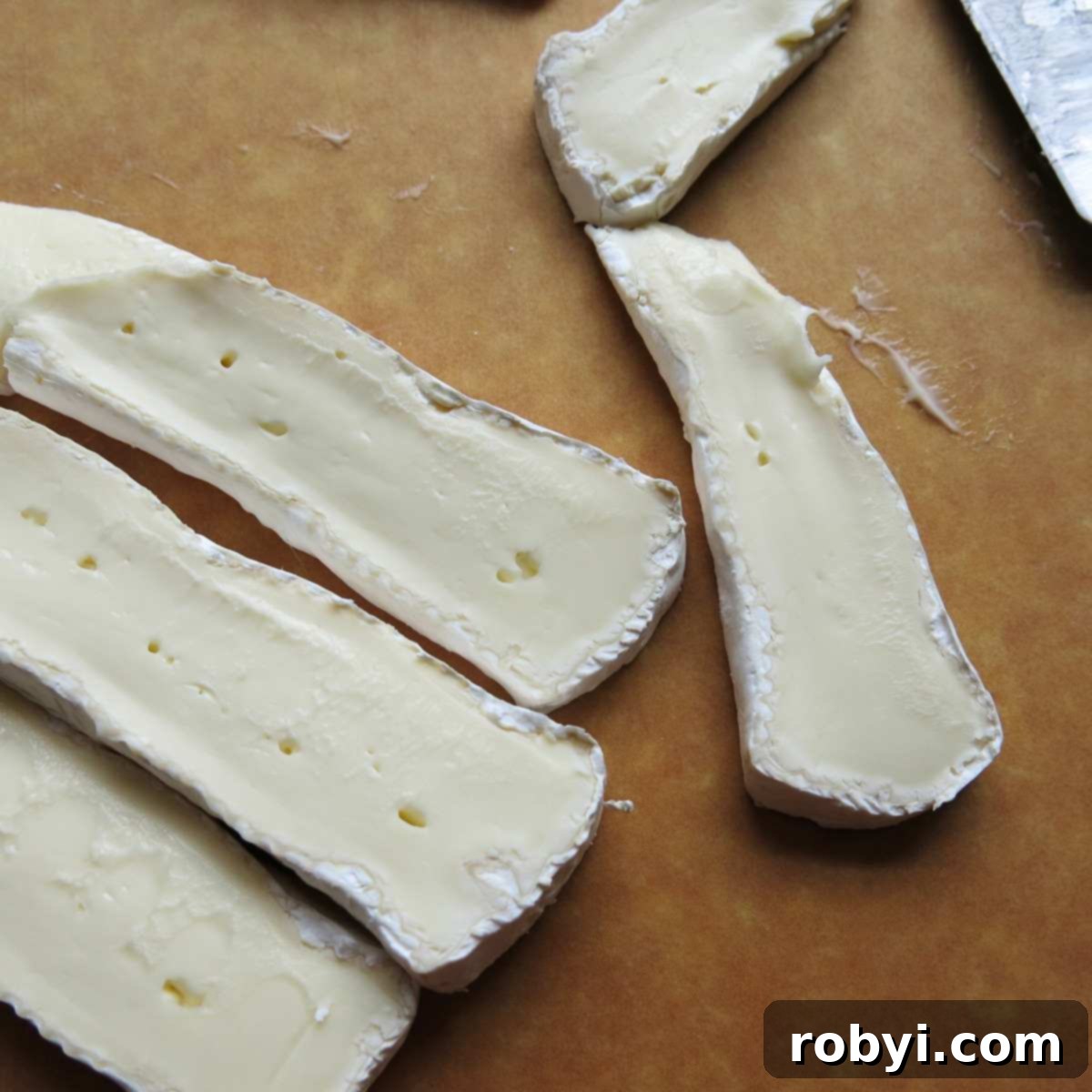 Perfectly sliced brie cheese ready for stuffing, displayed on a wooden cutting board.