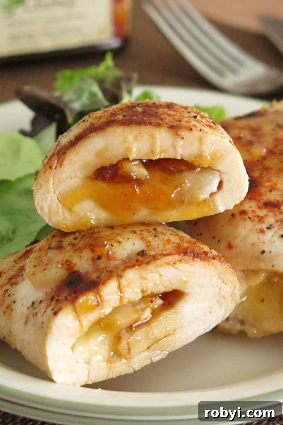 Stack of two beautifully baked chicken roulades, with melted brie and mango chutney visible, served on a white plate.