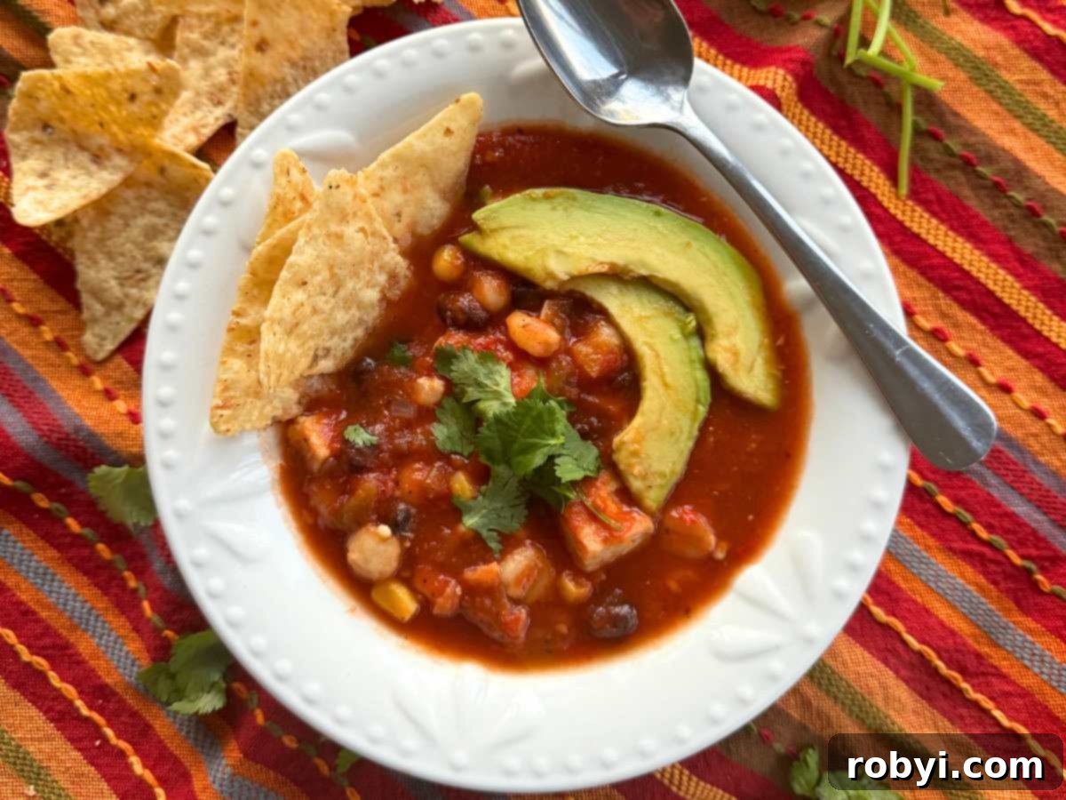 A vibrant bowl of chicken tortilla soup, generously topped with fresh avocado slices and crispy tortilla chips, presented with a spoon.