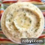 Host a Friendsgiving Feast for Less 8 Creamy crock-pot mashed potatoes with cream cheese and sour cream in a serving bowl with pools of butter, and chives on top.