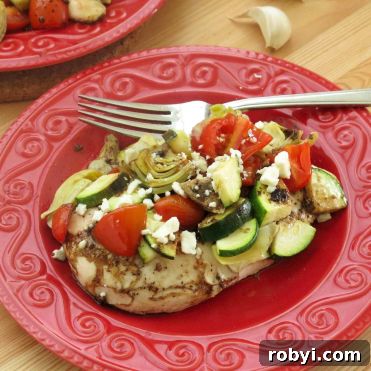 Tek Kapta Pratik Akdeniz Fırın Tavuğu 2 A serving of Mediterranean chicken bake with zucchini, artichokes, tomatoes, and balsamic vinaigrette on a plate with a fork, ready to be enjoyed.