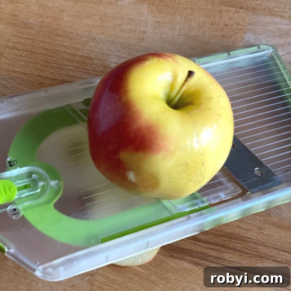 Homemade Crispy Apple Chips 3 Apple placed on top of a mandoline slicer with the core stem showing.