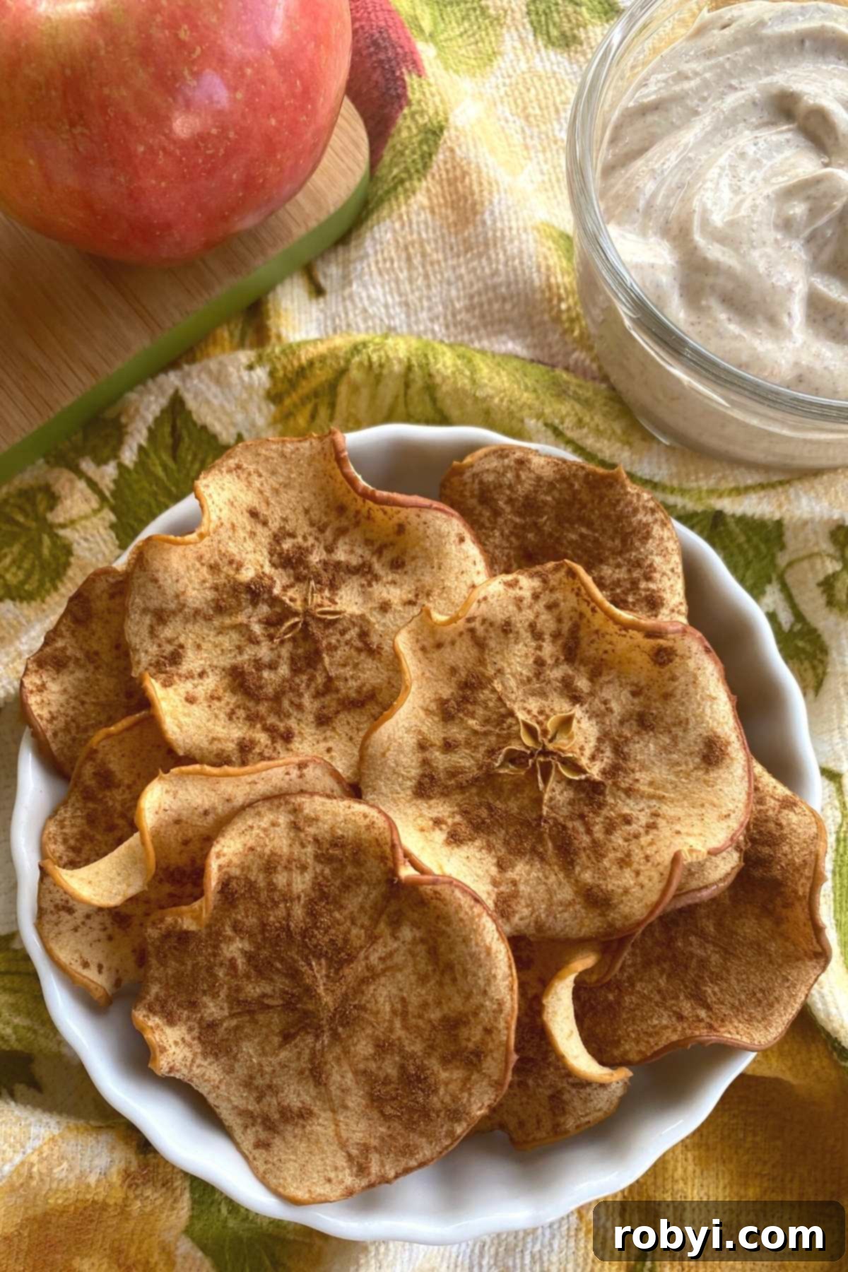 Homemade Crispy Apple Chips 8 Baked apple chips with cinnamon in a bowl with yogurt dip behind it.
