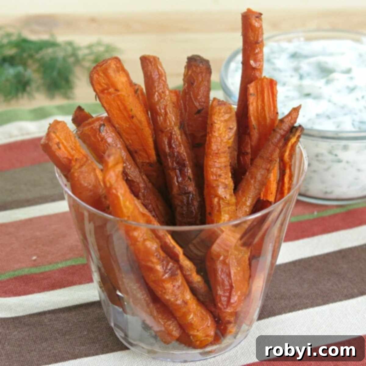 Crispy carrot fries served in a container with a creamy yogurt dipping sauce in the background.