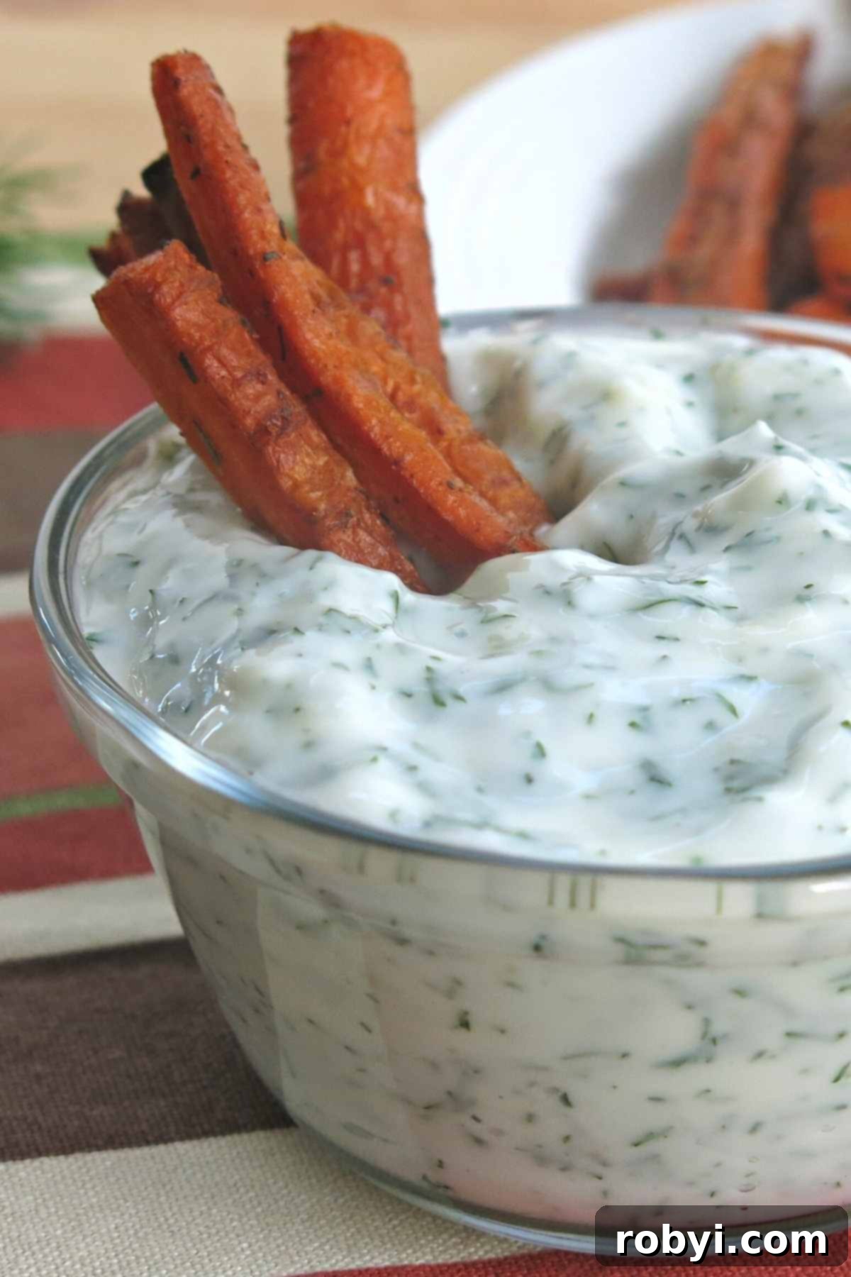 Several perfectly cooked carrot fries standing upright in a small bowl of creamy yogurt dip, ready to be enjoyed.