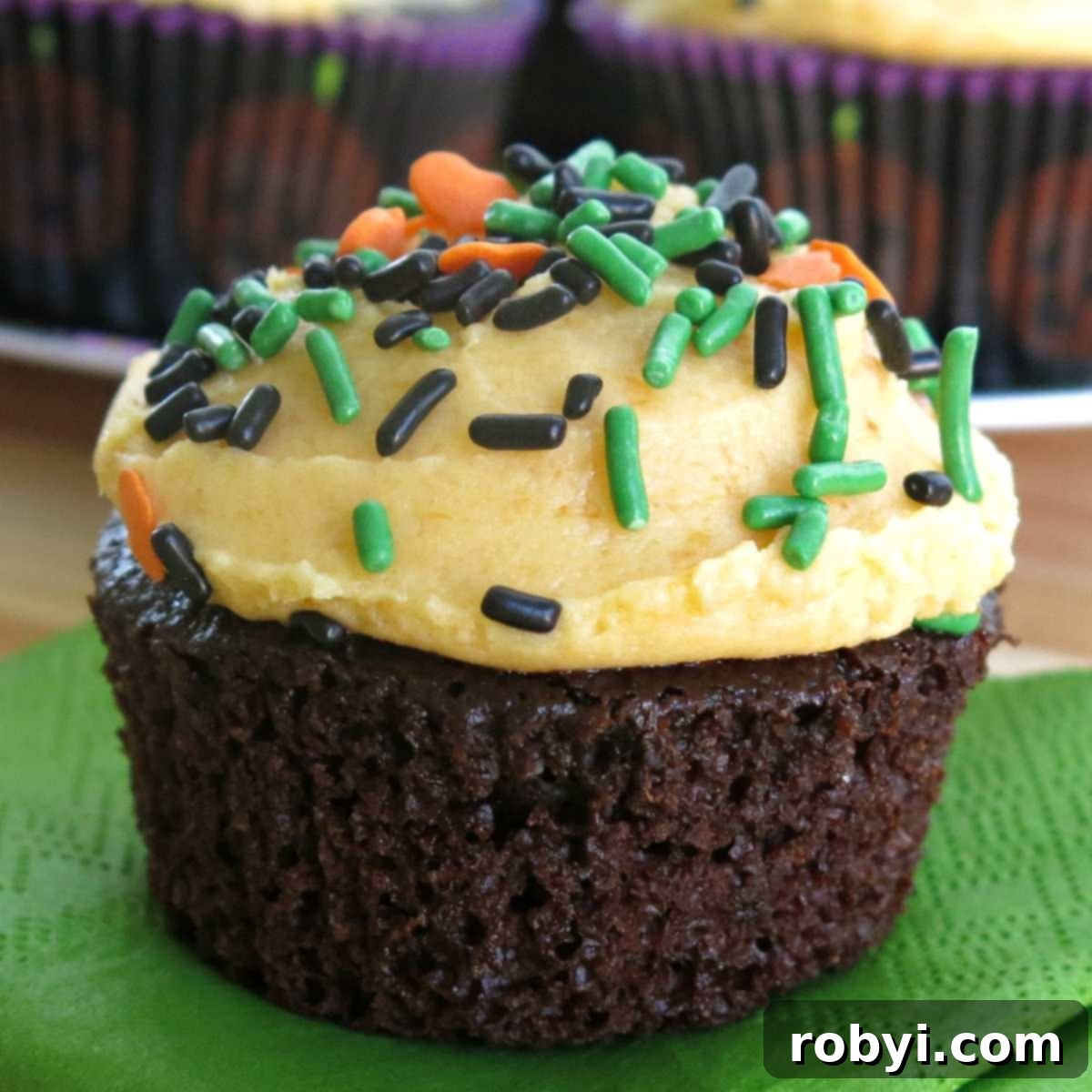 Chocolate pumpkin cupcakes with pumpkin buttercream frosting topped with green, chocolate and orange sprinkles.