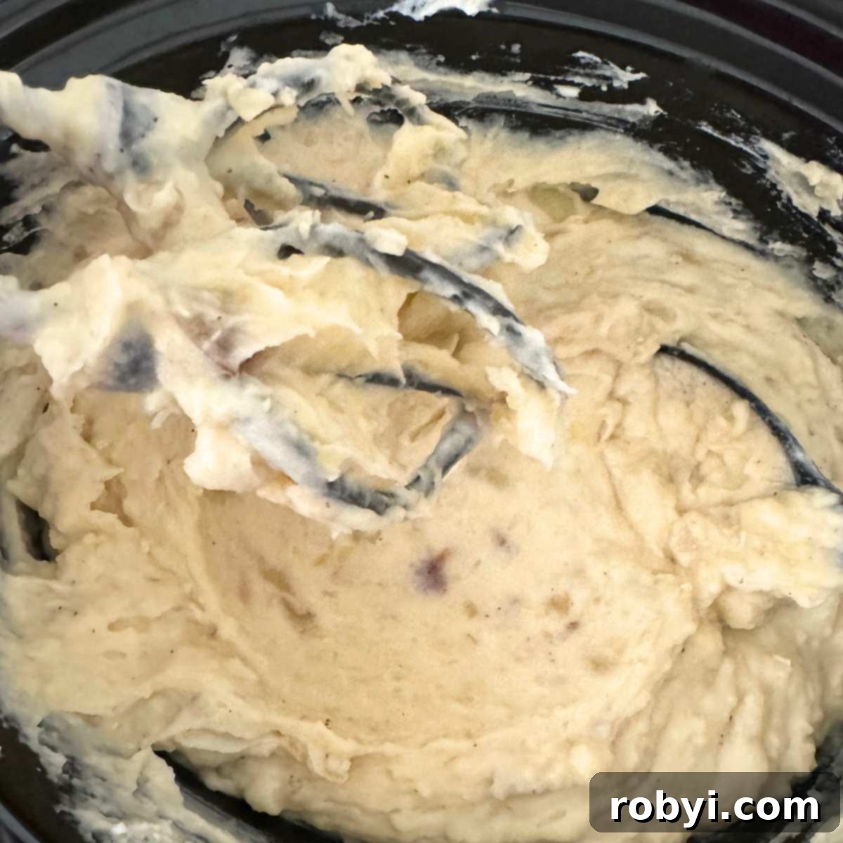 Electric beaters inside the crockpot with creamy mashed potatoes.