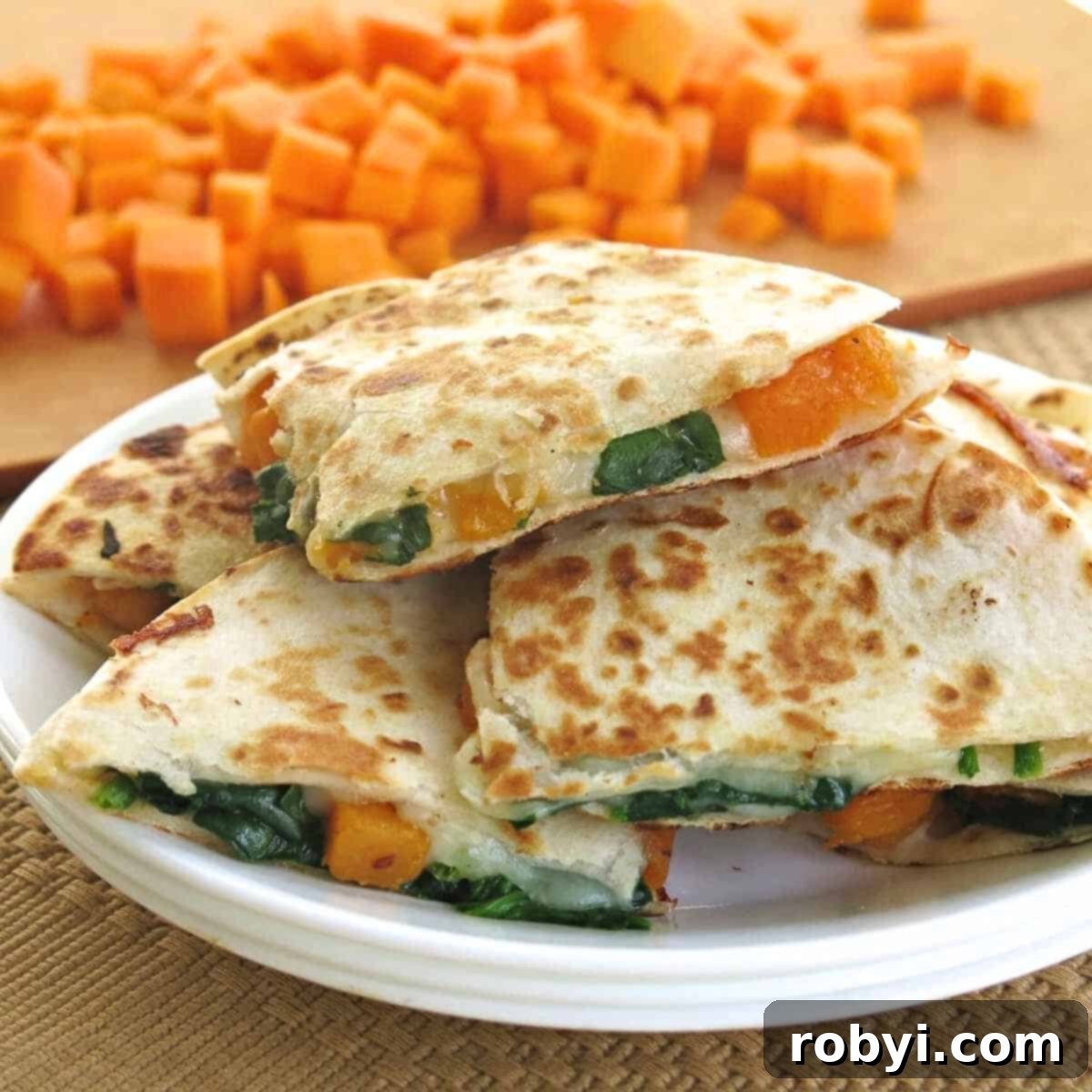 A vibrant plate of golden-brown butternut squash quesadillas, cut into triangles, with a scattering of fresh herbs. Cubes of roasted butternut squash and a rustic cutting board are visible in the background, hinting at the wholesome ingredients.
