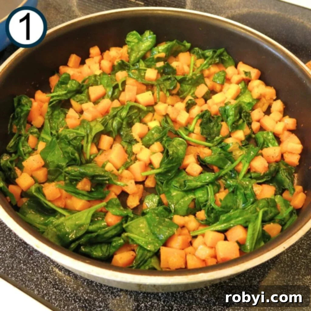 Butternut squash cubes and spinach being sautéed in a skillet with olive oil and butter, releasing aromatic steam.