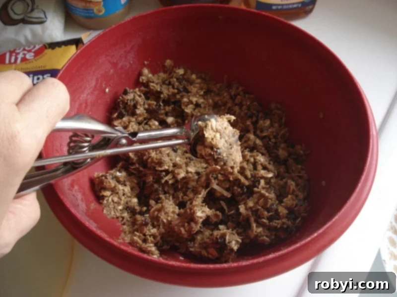 A small scoop lifting SunButter Energy Ball batter out of the bowl, demonstrating the rolling process.