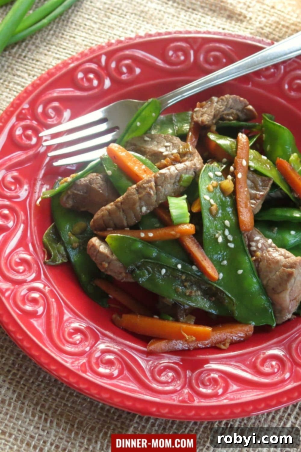 Sesame beef, snow peas and carrots on plate with fork.
