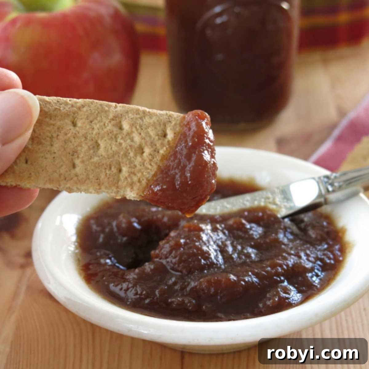 Naturally Sweet Slow Cooker Apple Butter 2 A bowl of low-sugar Crock-Pot apple butter next to a graham cracker topped with apple butter, showcasing its thick, rich texture.