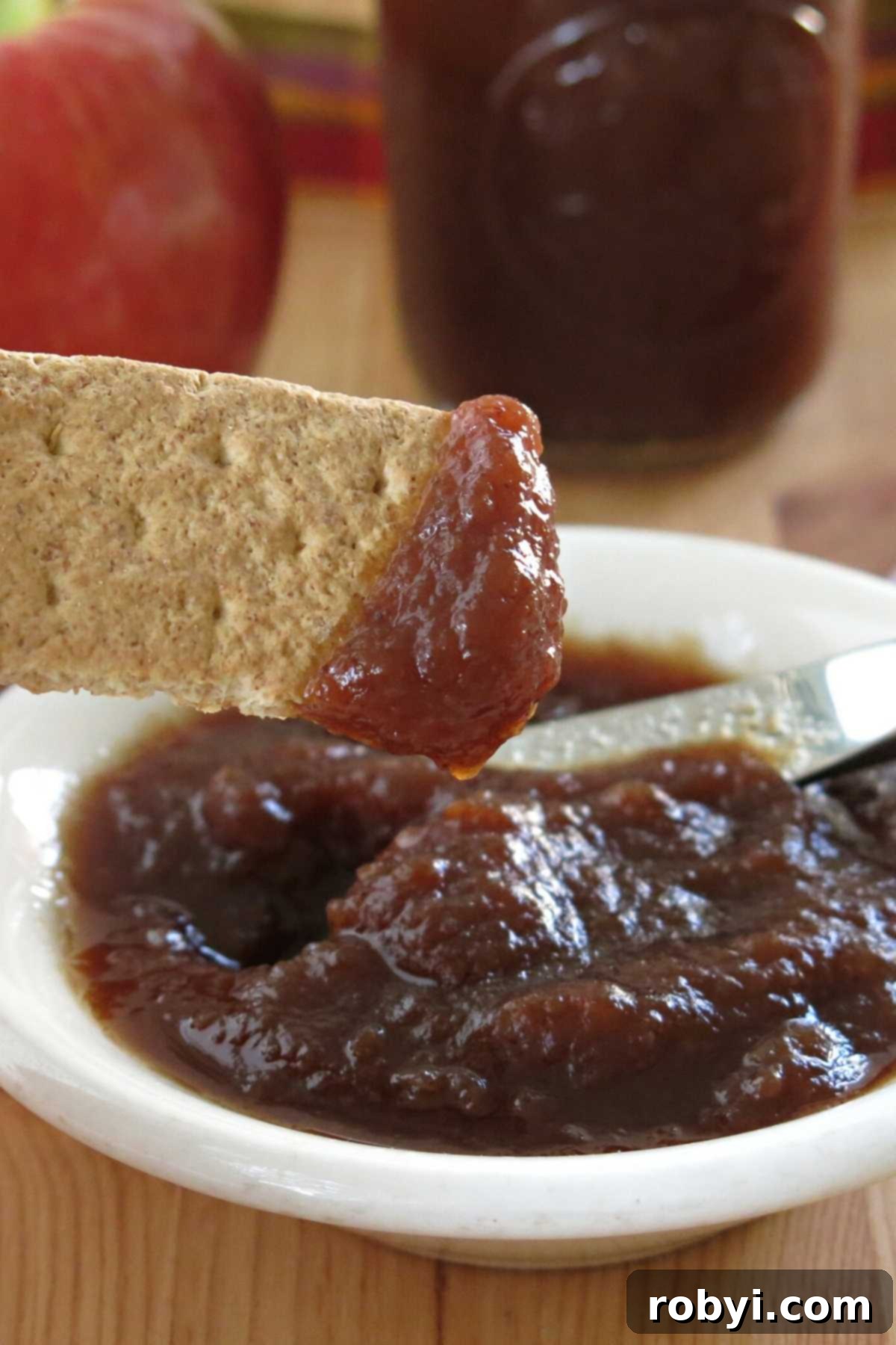 Naturally Sweet Slow Cooker Apple Butter 6 A bowl of healthy sugar-free apple butter alongside a graham cracker topped with apple butter, ready to be enjoyed.