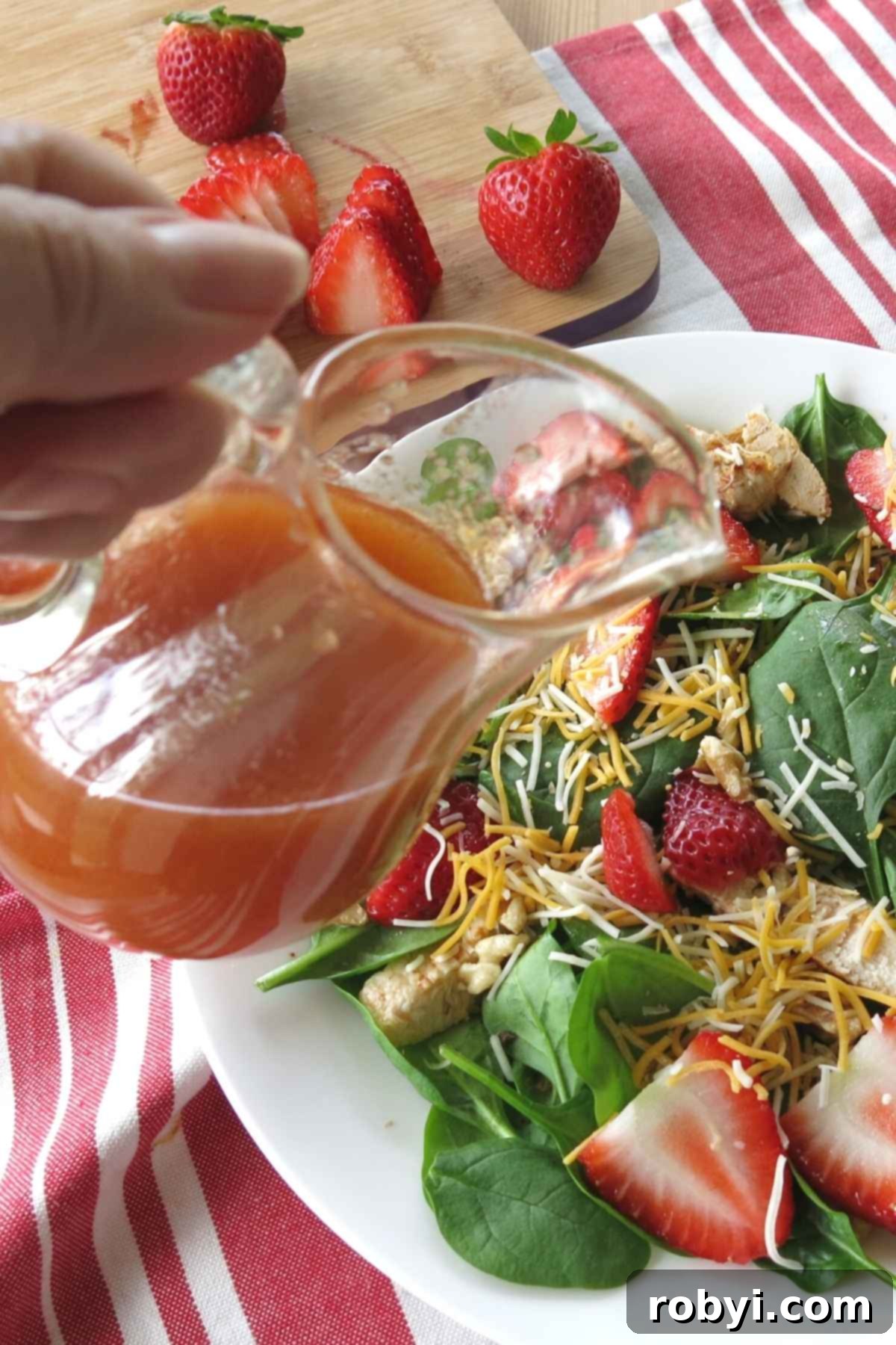 A hand gently pouring the vibrant Sweet Red Wine Vinaigrette Dressing over a fresh strawberry salad, illustrating the perfect application of this homemade dressing.