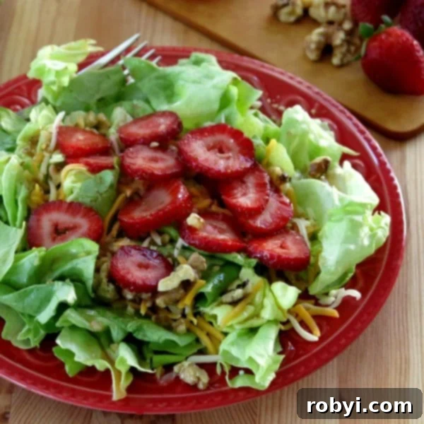 A vibrant salad generously dressed with Sweet Red Wine Vinaigrette Dressing, served on a white plate with mixed greens, strawberries, and nuts clearly visible.