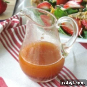 Sweet red wine vinegar dressing in a serving jar with strawberry salad behind it.